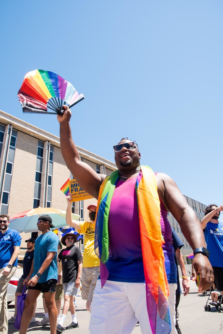 Iowa City Mayor Bruce Teague waves his rainbow fan as parade onlookers cheer. He is the first openly gay, Black mayor of Iowa City. 