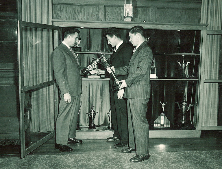 black-and-white image of men looking at trophies in Quadrangle lounge
