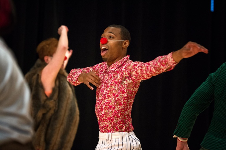Theatre student in a bright blouse wearing a red clown's nose dances.