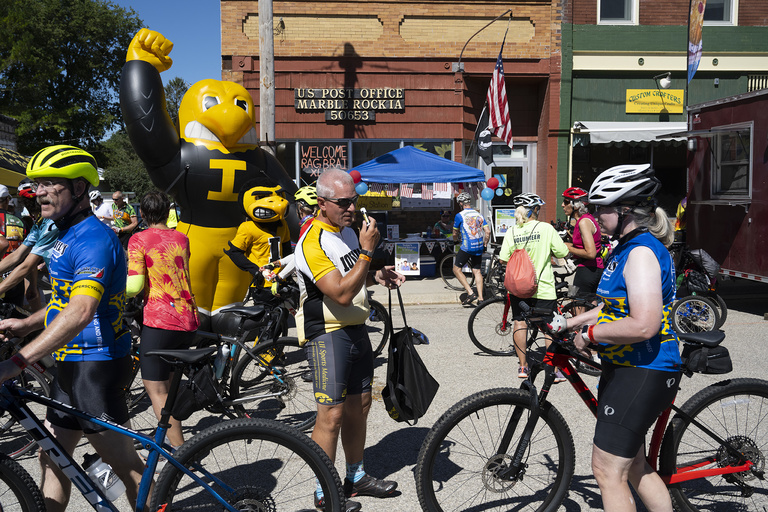 Mike Shaffer, a member of the official team representing the University of Iowa, hands out sunscreen to riders passing through Marble Rock on Thursday, July 28.