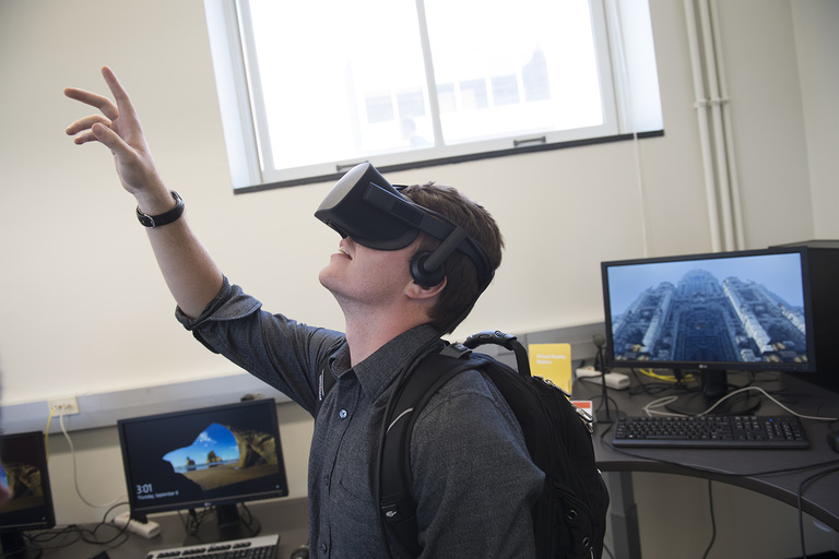 Student with virtual reality goggles reaching up into the air