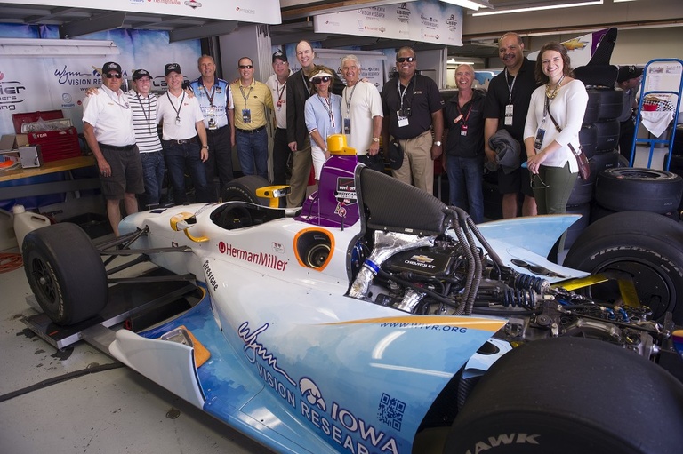 Team members and sponsors with the car in the garage.
