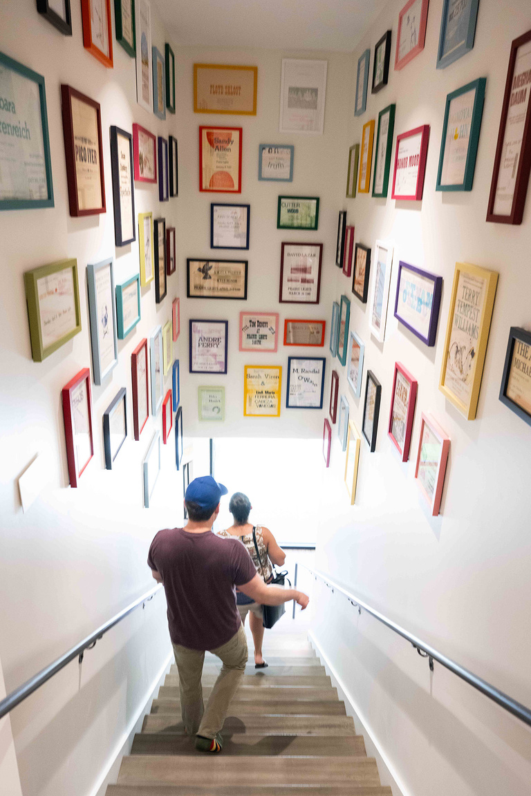 two people walk down a stairwell that features posters that promote readings from days gone by