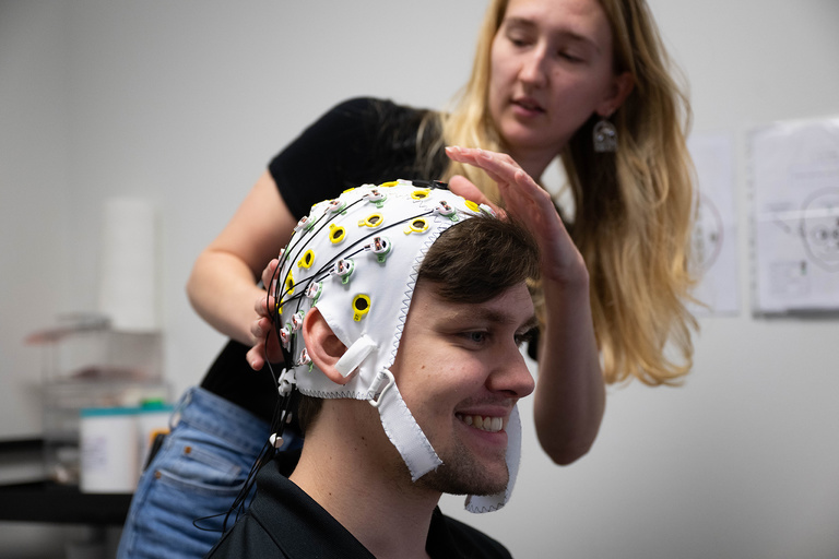 Researcher outfits participant with an electroencephalography (EEG) cap, or brain cap, a device that monitors electrical activity in the brain by using sensors attached to the scalp