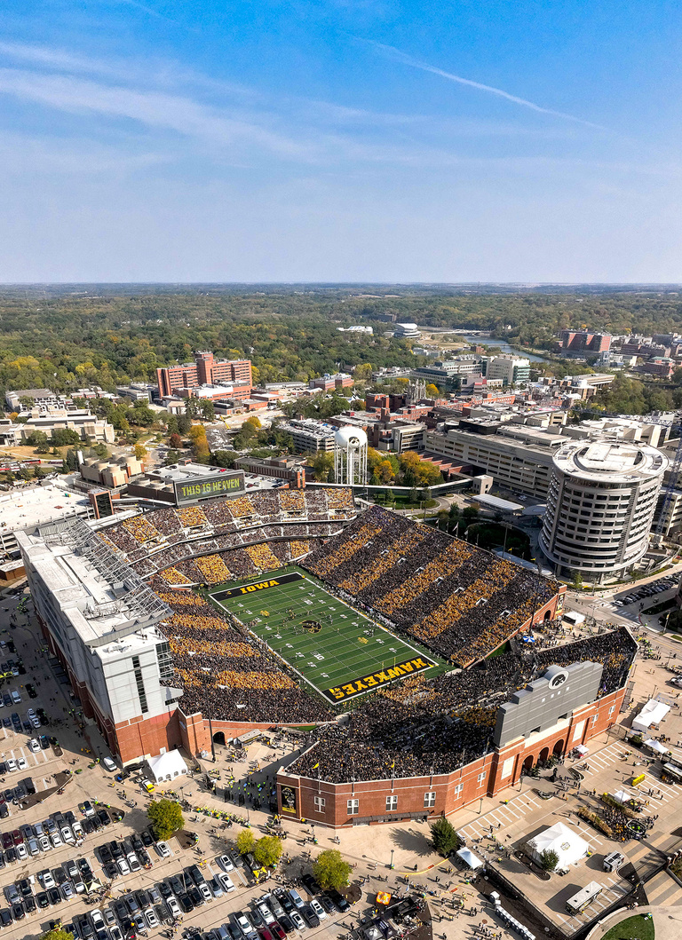 an aerial view of Kinnick Stadium during a football game; fans coordinated their apparel so that sections of the stadium appear to have alternating black and gold stripes