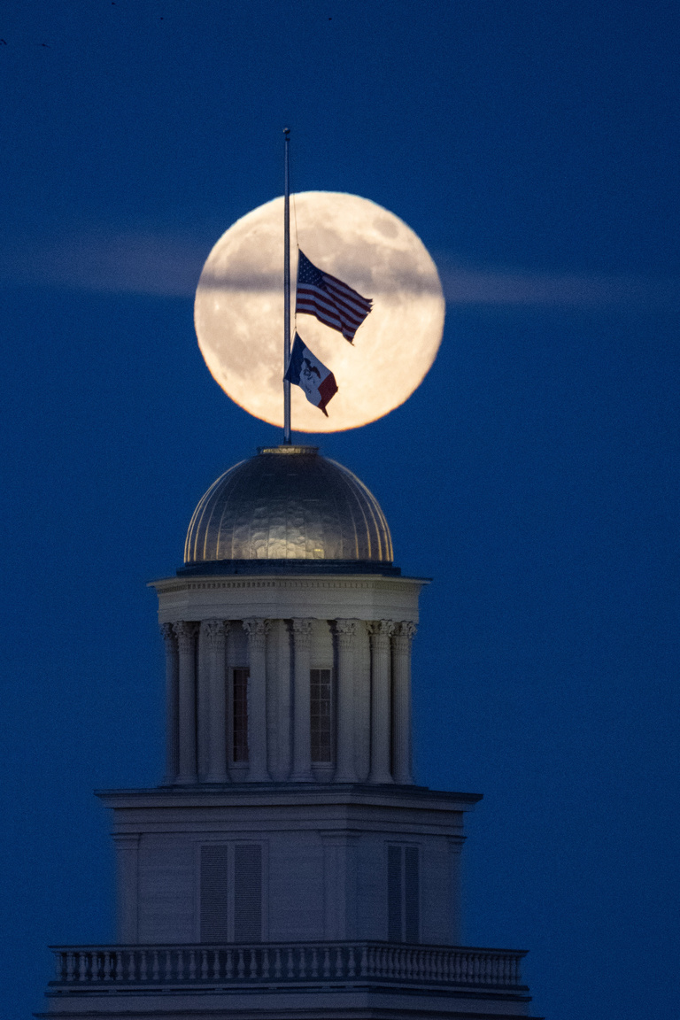 Flags fly on top of Old Capitol with a full moon in the background