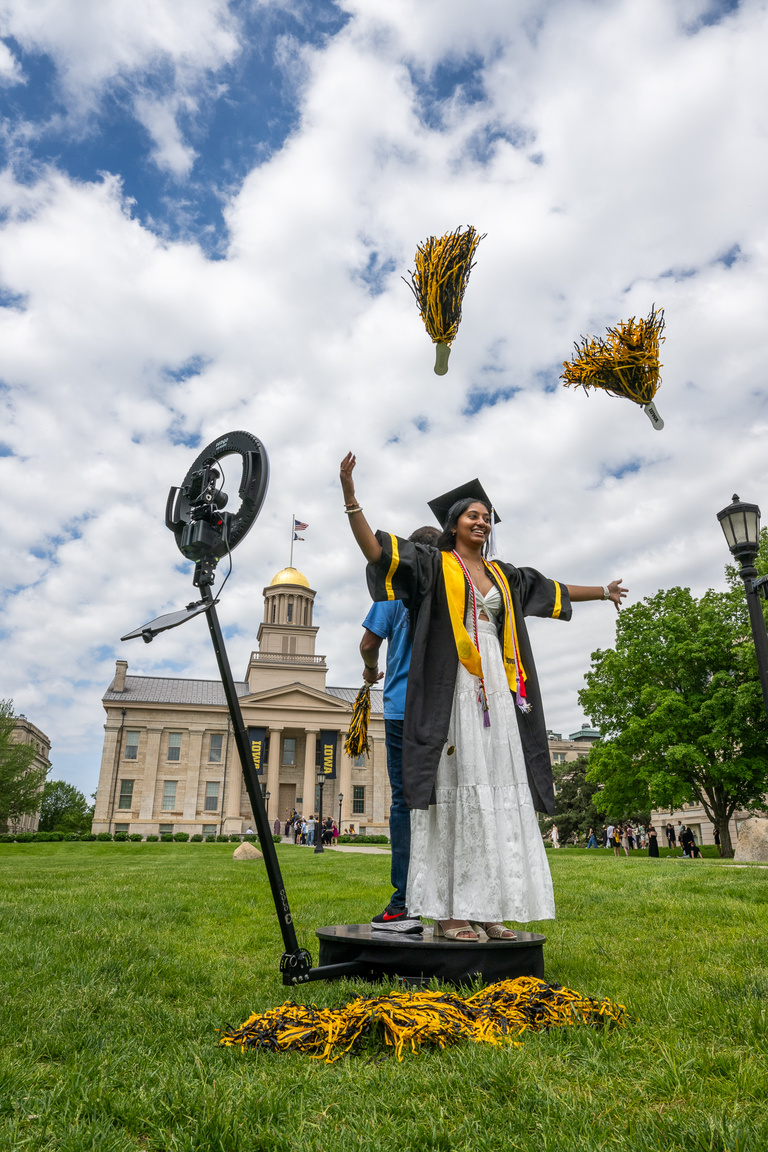 A graduate throws pompoms in front of Old Capitol