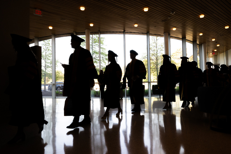 The silhouettes of graduates lining up inside Hancher Auditorium