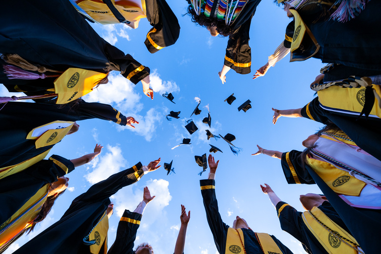 A circle of graduates throws their caps into the air