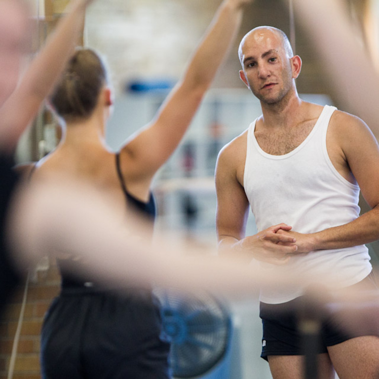 A male dance instructor watching dancers in the foreground.