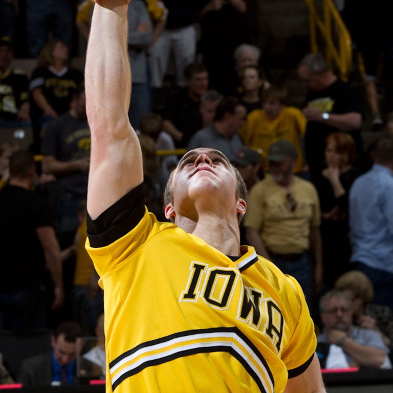An Iowa male cheerleader holds another cheerleader above his head, you can see only her feet in the upper left corner.
