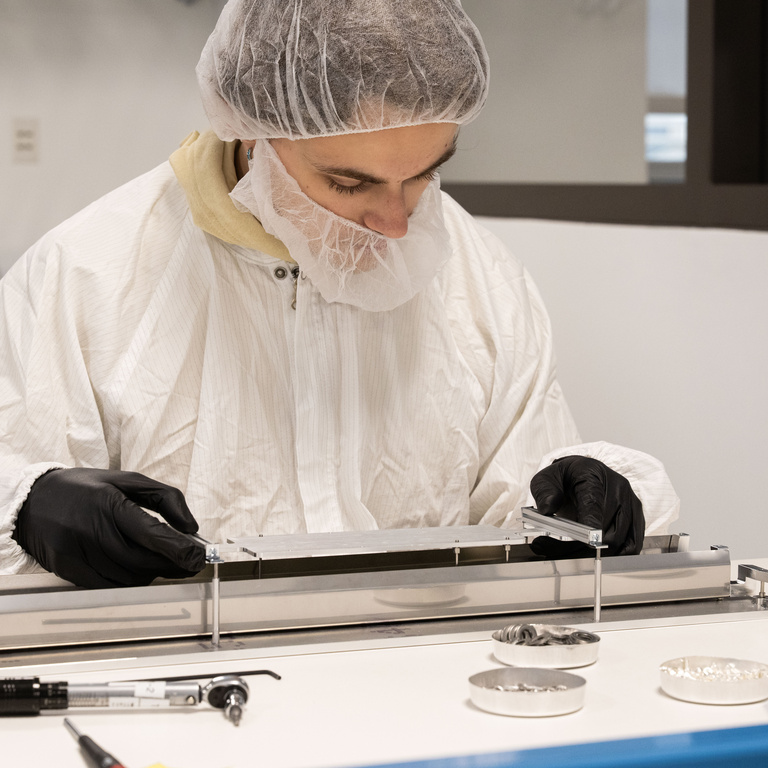 Parker Kovar, a physics and math major from Omaha, Nebraska, inserts and secures an elevated platform on which an electronics circuits board will be situated. The board will supply power to a photon (particles of light) detector for the DUNE experiment, an international effort to study neutrinos, a highly elusive particle that could explain how the universe formed and how it’s evolved.