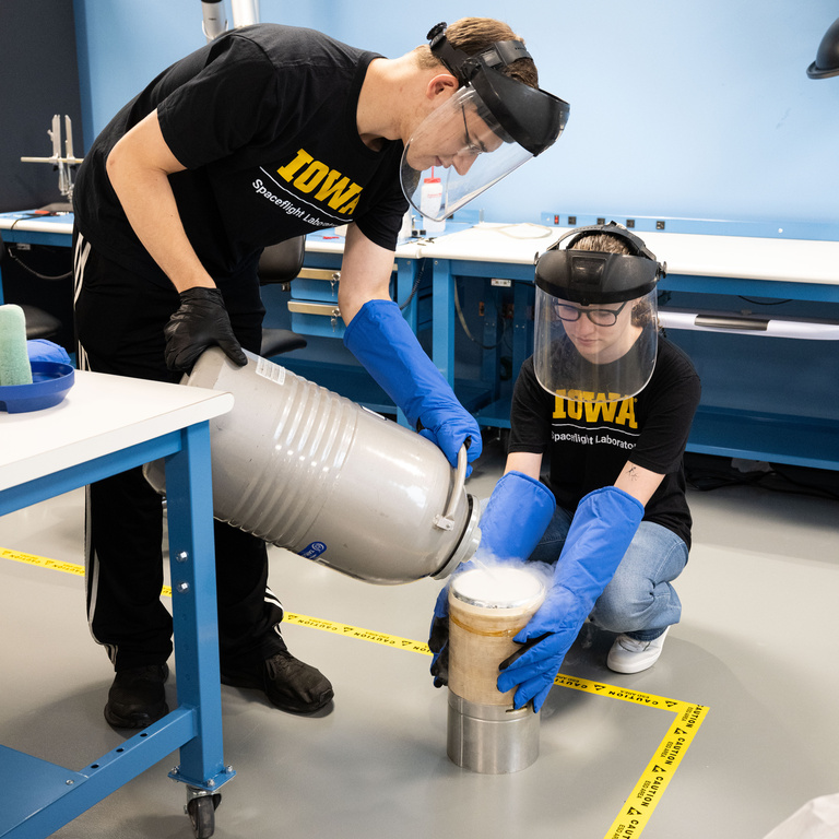 University of Iowa students Bryson Kinnan (left) and Sydney Tune pour argon, which is chilled in liquid form at -300 degrees Fahrenheit, as a demonstration for media who toured the lab where UI students are building and testing hundreds of electronic circuits and protective boxes for DUNE, an international effort to study neutrinos, a highly elusive particle that could explain how the universe formed and how it’s evolved.