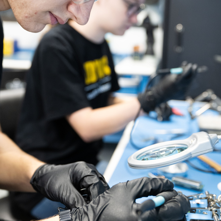 University of Iowa students Bryson Kinnan (foreground) and Sydney Tune (background) solder components for an electrical circuit board. The boards will supply power to a photon (particles of light) detector for the DUNE experiment, an international effort to study neutrinos, a highly elusive particle that could explain how the universe formed and how it’s evolved.