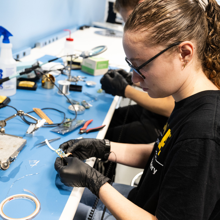 Sydney Tune, a senior from Strafford, Missouri majoring in physics and astronomy, examines an electronics circuit board. UI students assembled and tested 350 electronics circuit boards that will be used for DUNE, an international effort to study neutrinos, a highly elusive particle that could explain how the universe formed and how it’s evolved.