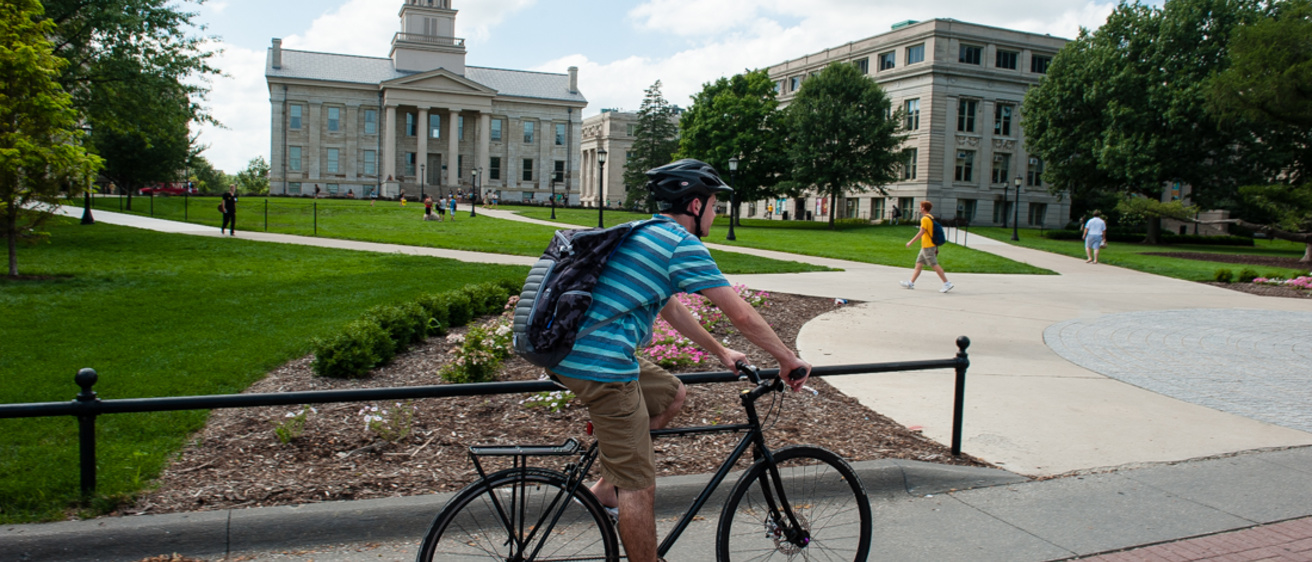 A student rides a bike across campus in front of the UI Pentacrest.