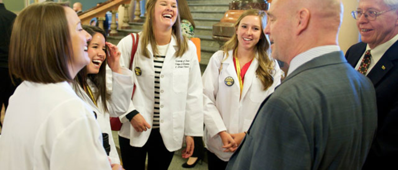 Students in white coats chat with a couple of men in suits