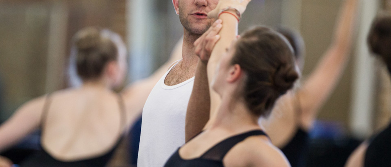 Male dancer holds the arm of a younger female dancer, assisting her ballet form