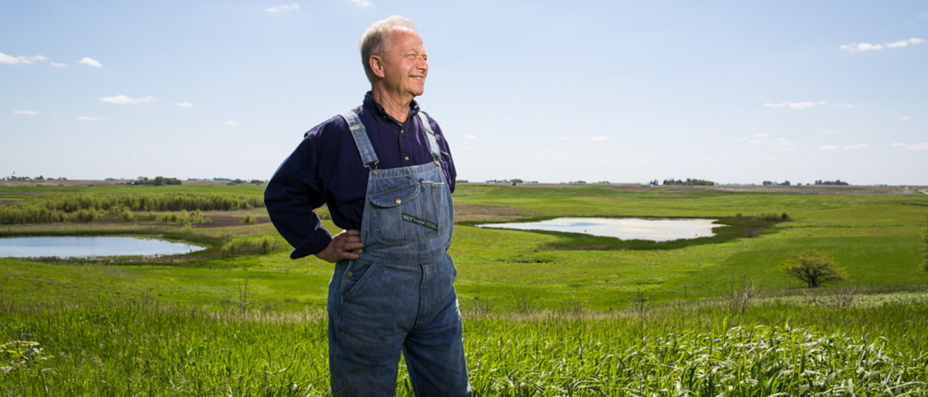 A farmer in bib overalls standing in a field of grass