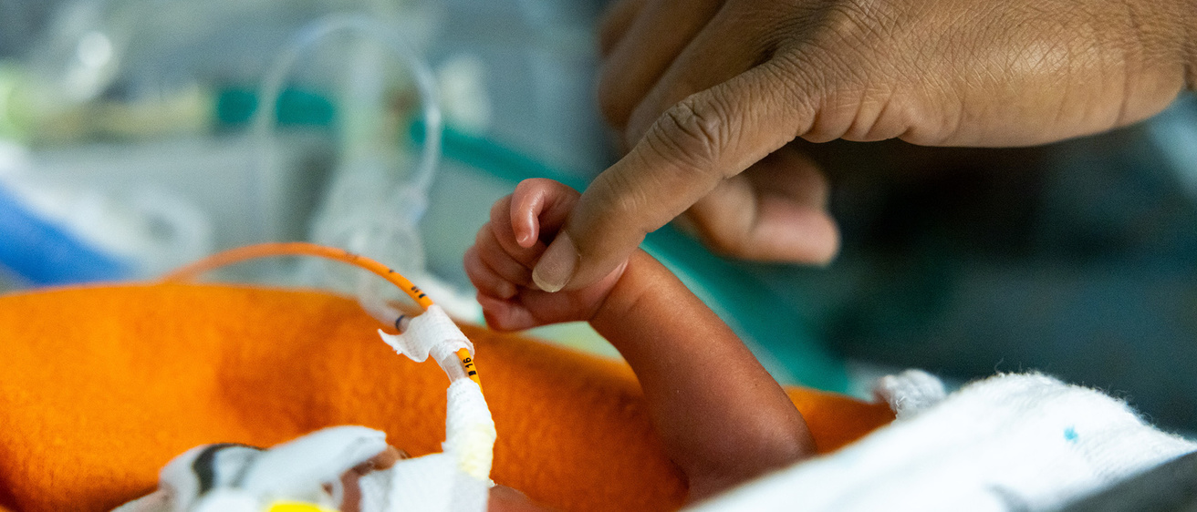 a preterm baby's hand touches an adult's finger