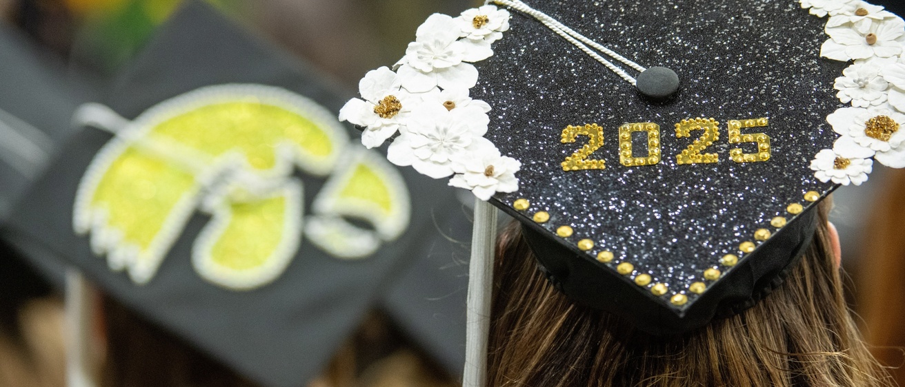 A close-up of a graduation cap adorned with glitter, sequins and flowers.