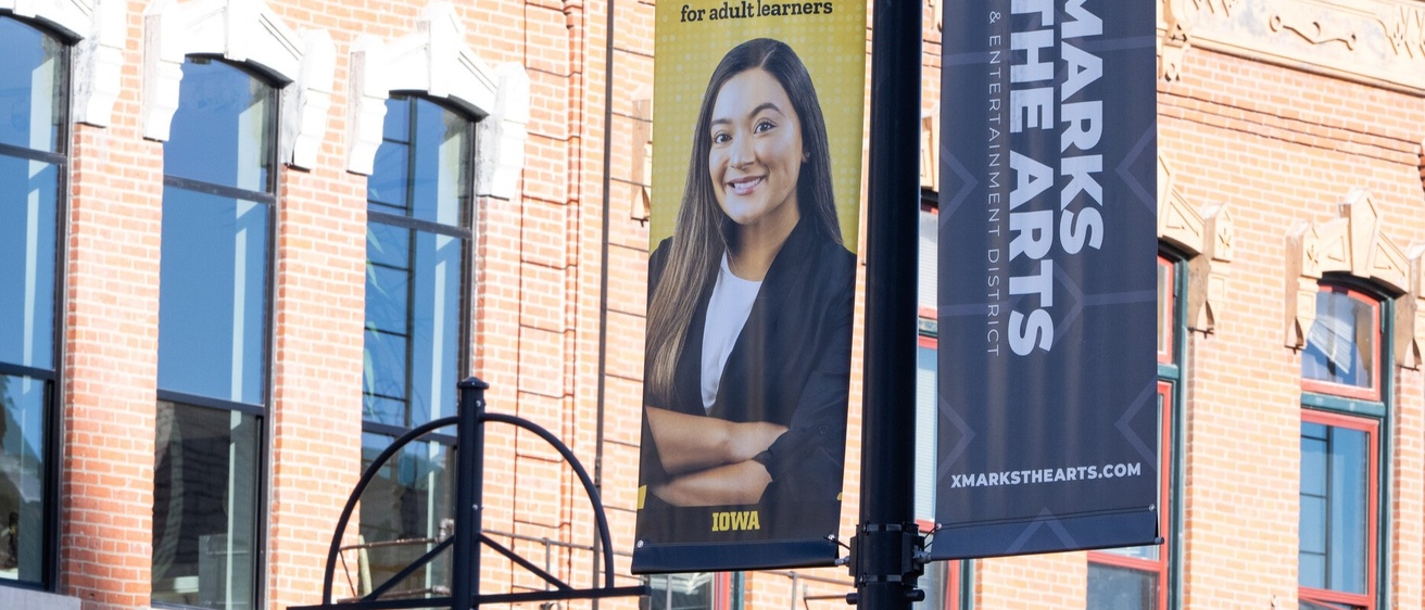 A banner on a light post in downtown Iowa City that is decorated with a photo of a Dare to Discover student