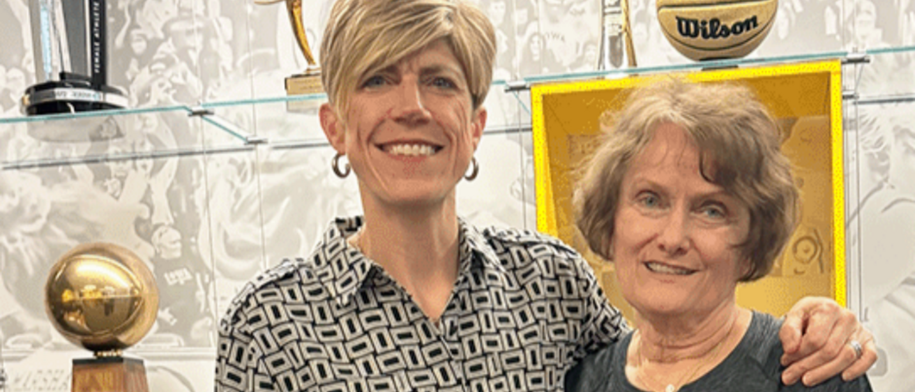 Iowa Women's Basketball coach Jan Jensen and UI alum Sheryl Stoll standing in front of a case of basketball trophies.