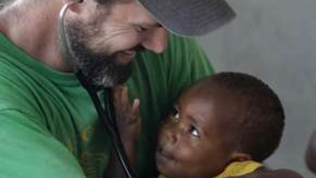Dr. Chris Buresh cuddles a a Haitian youngster, Wendly Steven, 13 months old, who has severe scar tissue on his hand from grabbing a piece of firewood/
