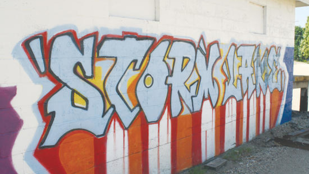 A graffiti sign on a building wall that spells out Storm Lake on top of white and red stripes.
