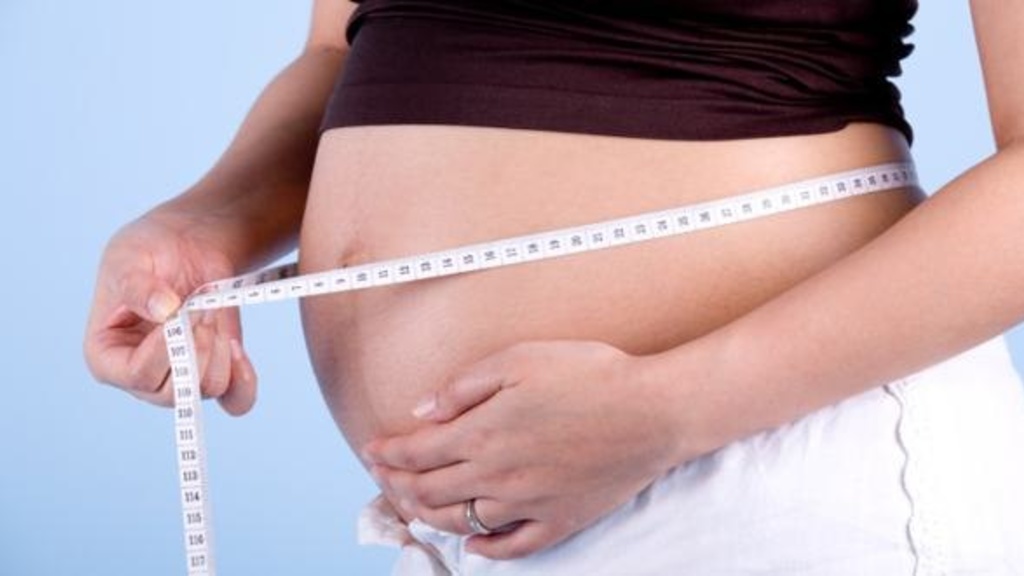 Image of a pregnant woman&#039;s stomach with a tape measure around it