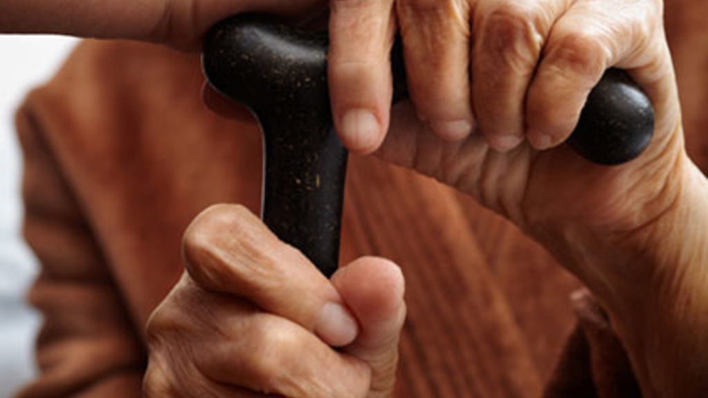 adult hand touches elderly hands on a cane