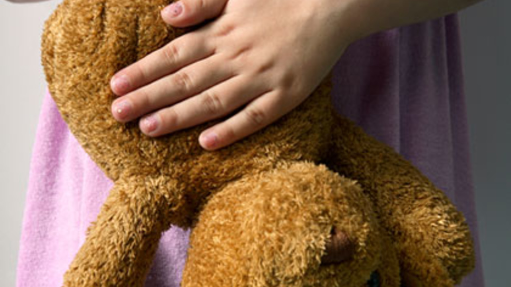 child clutching an upside down teddy bear