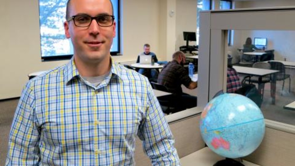 Matt Gilcrest poses by a globe in a TILE classroom