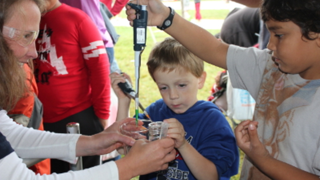 An iExploreSTEM volunteer teaches children how to use a pipette at the festival co-produced by the State Hygienic Laboratory and the Iowa Mathematics and Science Education Partnership on Sept. 18, 2011.