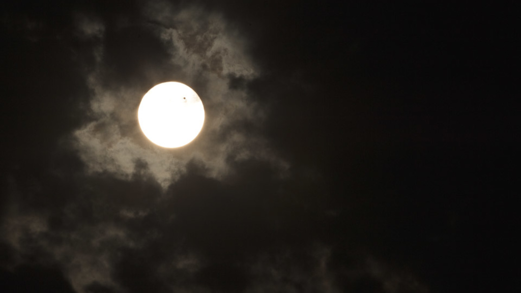 Venus as a small dot in front of the Sun peeking through the clouds